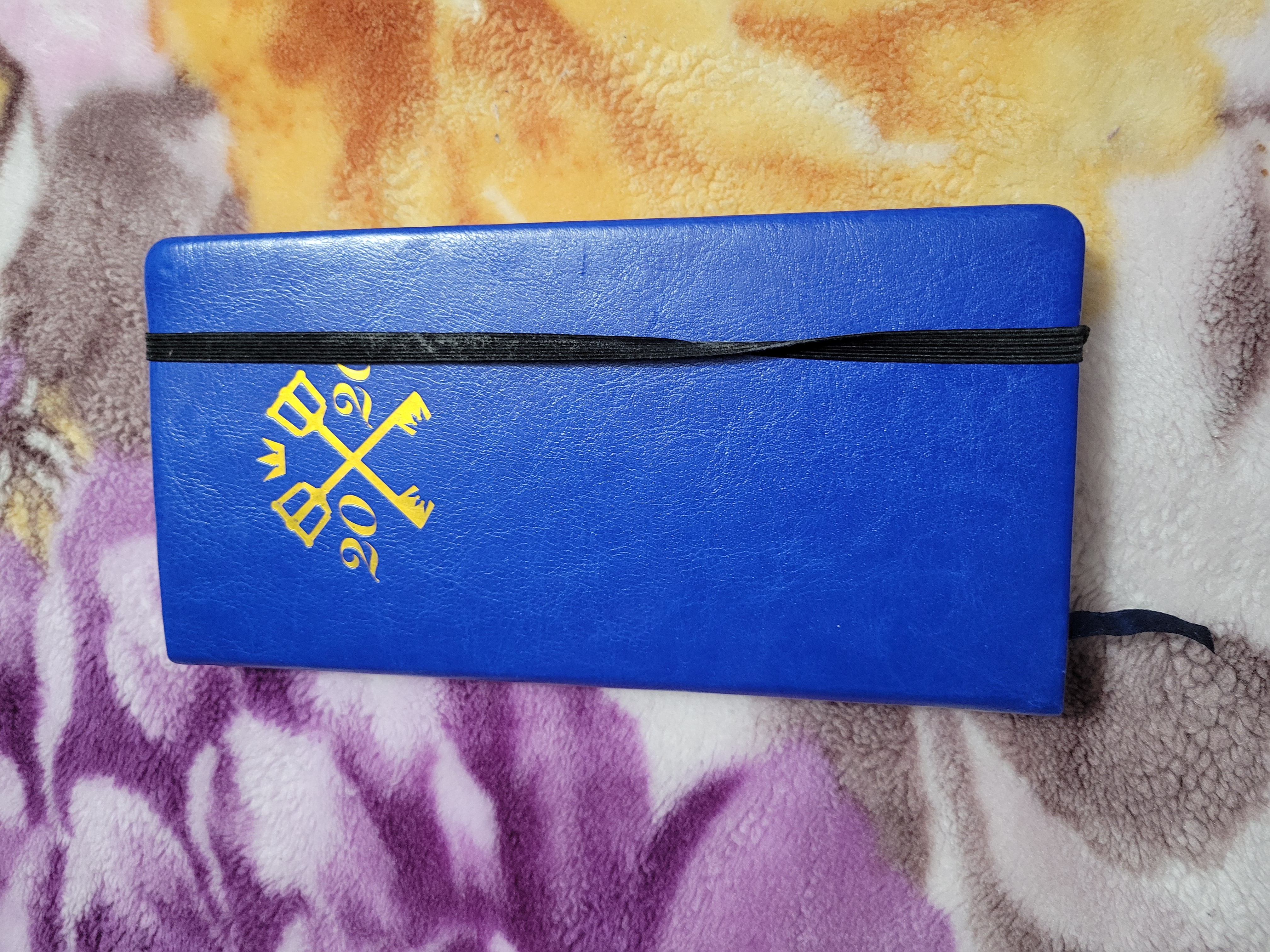 Front of moleskin style Kingdom Hearts blue weekly plan that has the year 2020 with two keyblades crossing in the middle, a crown on top and a black strap holding it closed.